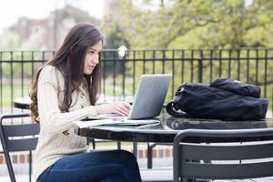 键入在膝上型计算机的大学生在室外桌上