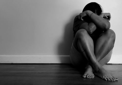 Woman sitting on floor, ankles crossed and her head in her arms