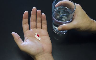 拿着三个药片和一杯水的手反对黑背景，拷贝空间