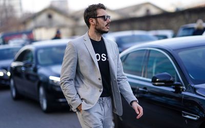 穿灰色衣服的白人和内衬衣内部。他有太阳太阳镜，在黑暗的汽车旁边行走