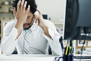 商人在办公桌上打电话，手放在额头上