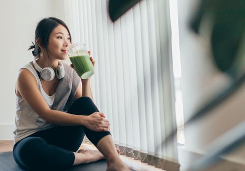 在瑜伽以后的年轻亚裔妇女饮用的绿色圆滑的人