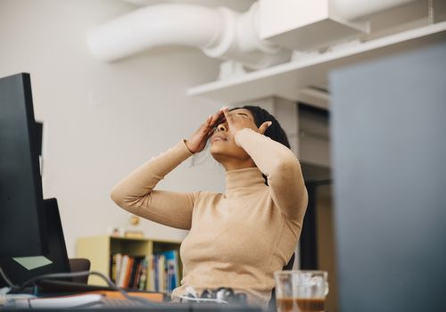 A stressed-out woman sits at her desk and rubs her eyes.