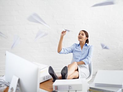 young businesswoman throwing paper planes while sitting at her desk