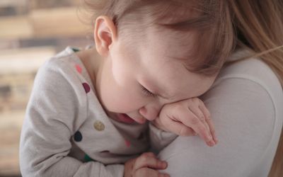 蹒跚学步的女孩靠在母亲的肩膀上哭泣