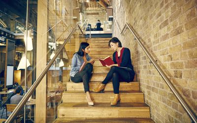 两个女同事在时髦，现代办公空间楼梯上工作。