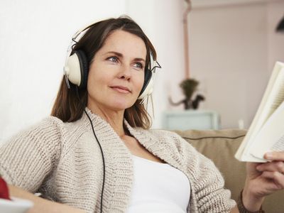 Middle-aged woman sitting on sofa, Listening to music and reading book