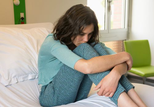 Female depressed patient sitting on the bed in a hospital ward