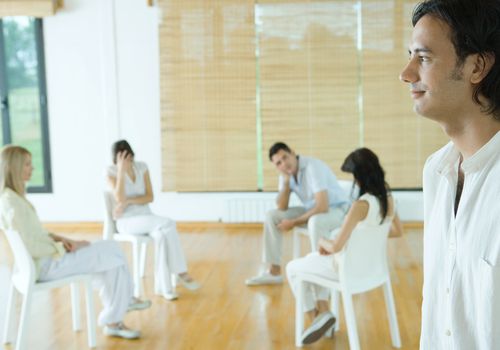 Group therapy session, man standing in foreground, smiling