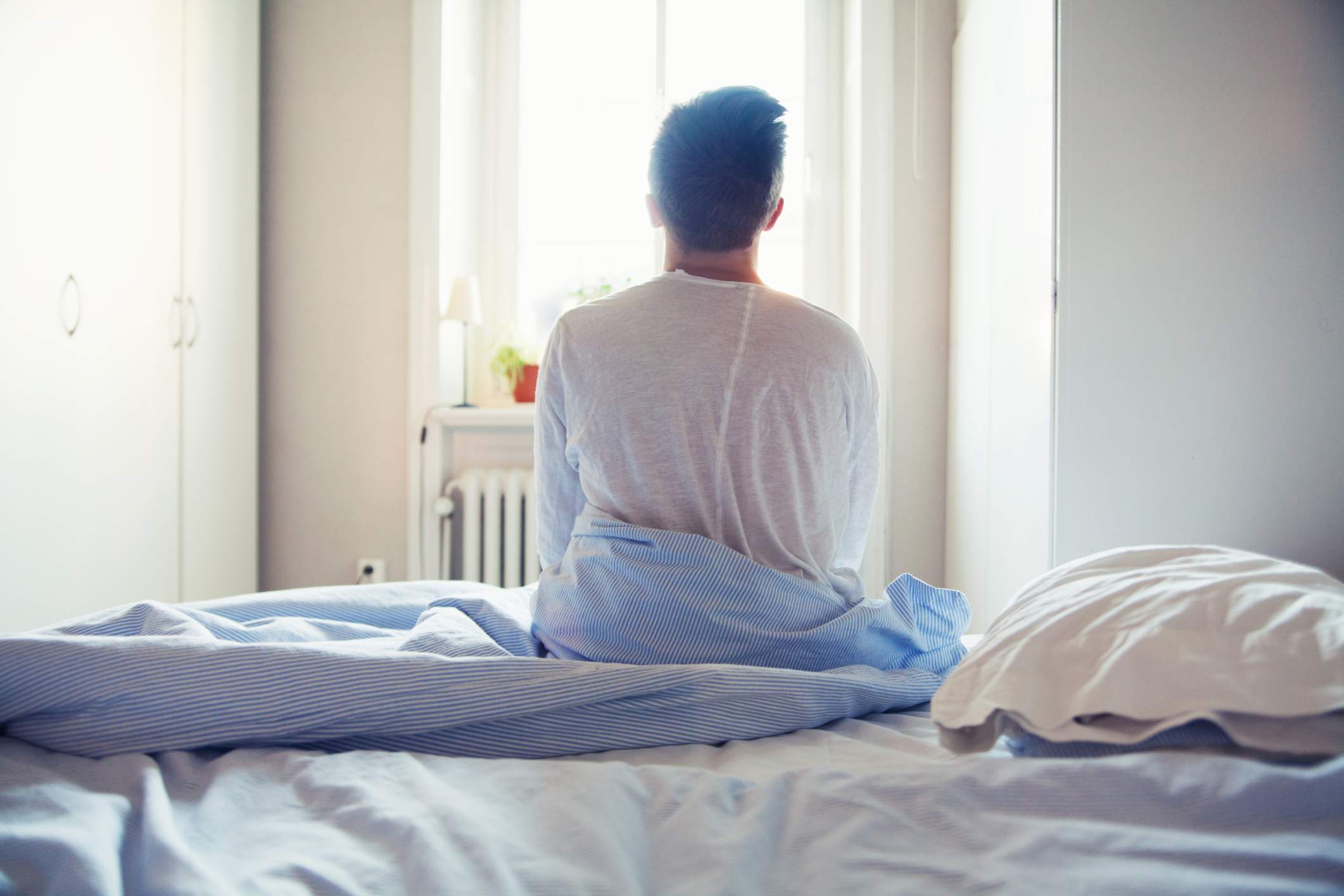 一个人坐在床上，看着窗户