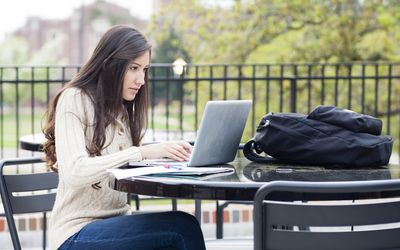 键入在膝上型计算机的大学生在室外桌上