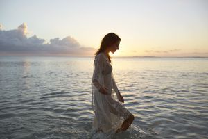 褐发女人穿着泳衣微笑和涉水在日落的海洋