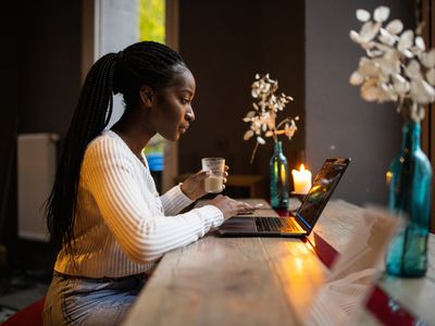 一位非洲裔美国妇女坐在电脑前，手里拿着鲜花和蜡烛
