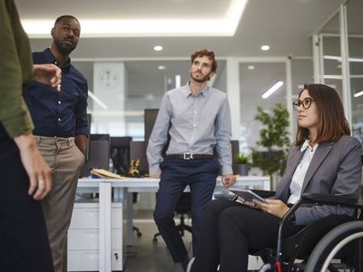 残疾人的女商人在轮椅与办公室同事聊天