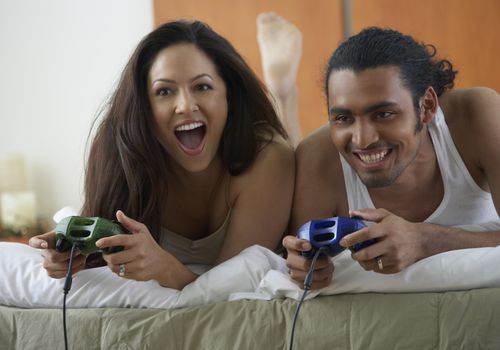 Couple laying on bed holding video game controllers