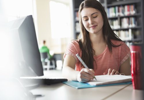 写在一本笔记本的女学生在计算机前面