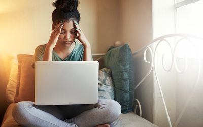 a young woman looking stressed out with her computer in her lap in bed