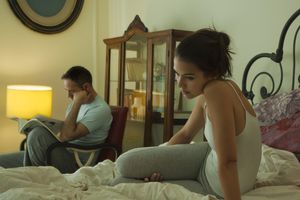 妻子独自坐在床上沉思，丈夫在背后看书