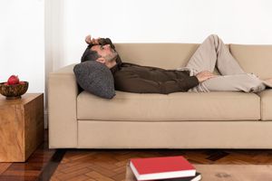 Side view of mature man lying on back on sofa hand on forehead, looking up