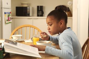 Girl sitting at breakfast table reading a book