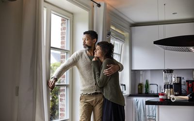 Pensive man staring out window with arm around woman