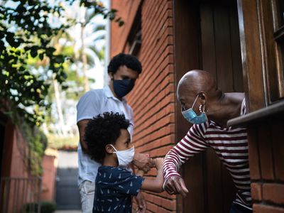 little boy wearing a mask bumping elbows with an older woman