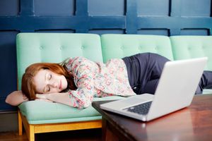 女人睡着在有膝上型计算机的沙发