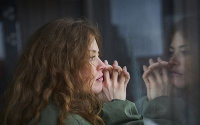 一个女人望着窗外，忧心忡忡。