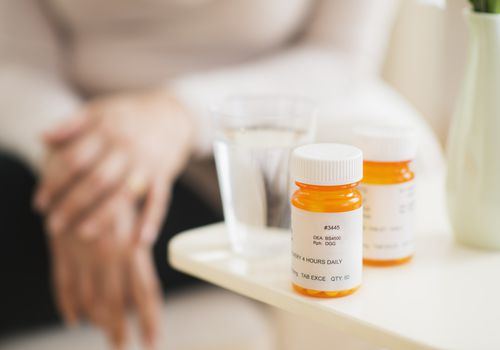 Two pill bottles and glass of water sitting on a table with woman in background