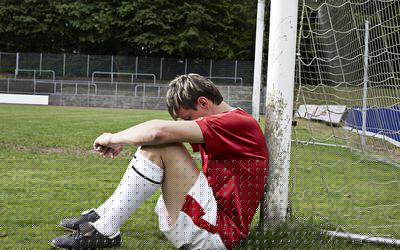 少年坐地面倾斜反对有头的足球目标岗位在他的膝盖