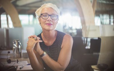 自信成熟的女人在现代办公她的办公桌上靠在