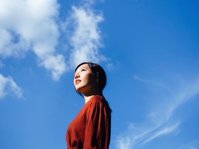 自信年轻的亚洲女性低角度肖像站在美丽的蓝天，仰望天空享受阳光。自由的天性。与自然的联系-库存照片