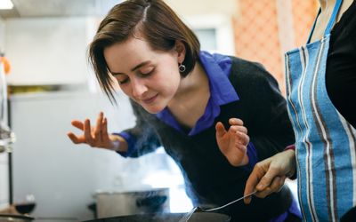 woman smelling food from a pan on the stove