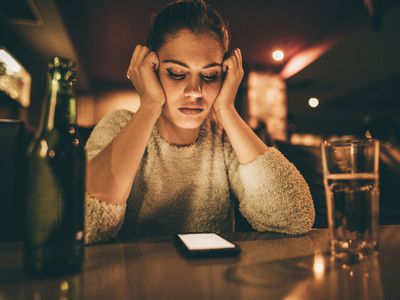 upset woman looking at cell phone on bar