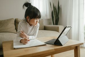 A young girl with black hair working on a computer with wireless headphones in.