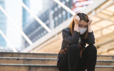 Tired looking woman sitting on steps wearing a mask.