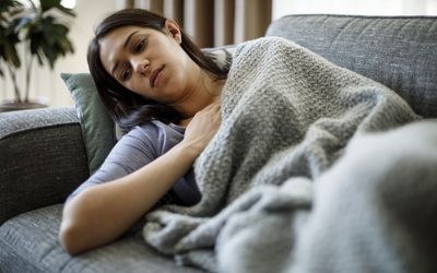 黑发的一个人抱着胸口，在毯子下铺设灰色的沙发。