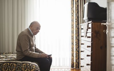 old man sitting on the bed looking sad