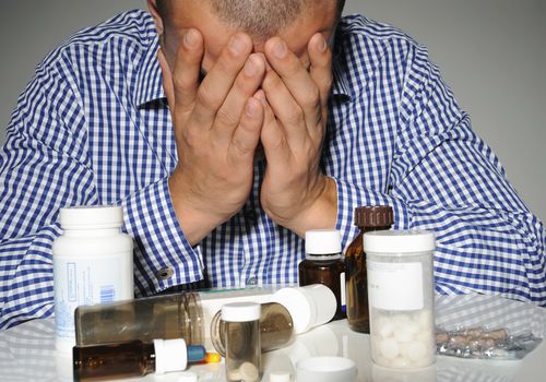 Man surrounded by medicine bottles, studio shot
