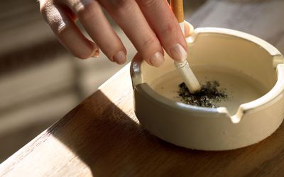 Hand holding cigarette in ashtray