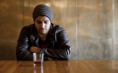 神情沮丧的男子端着一杯酒坐在桌旁