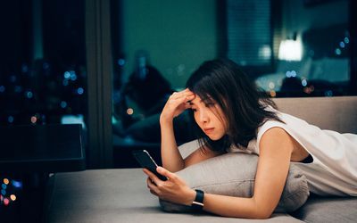 年轻的亚洲女商人工作到很晚，在家用手机查看工作电子邮件