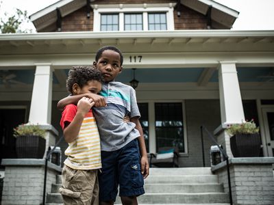 Two young children standing in front of their home