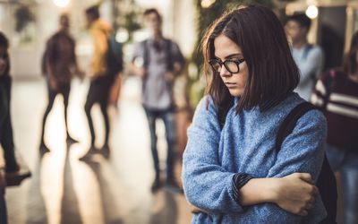A girl standing separate from a group with her arms folded.
