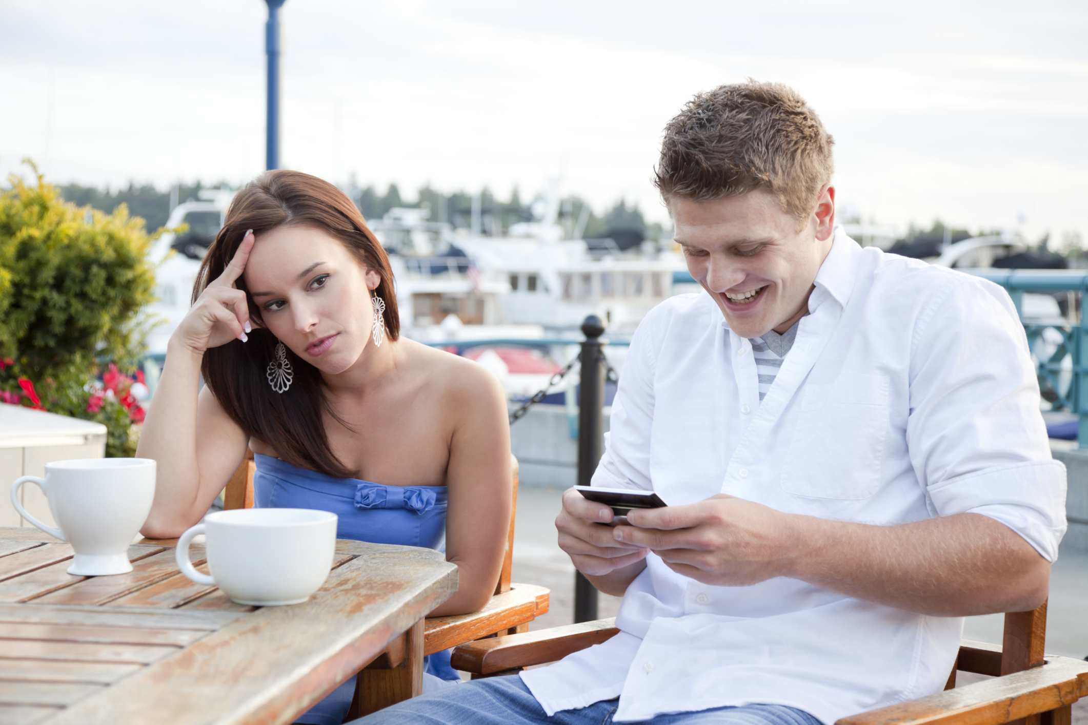 Young woman looking irritated by her date who is preoccupied with his phone