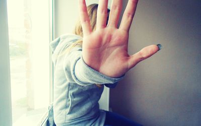 Woman sitting on window sill holding her hand up to the camera to block her face