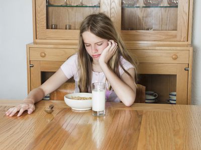 tween girl grimacing at bowl of cereal