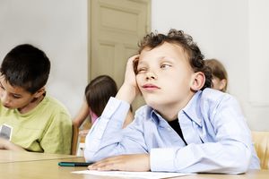 一个男孩坐在课堂，双手抱着头。