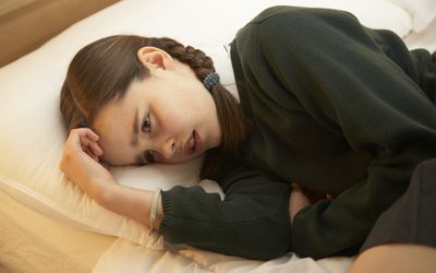 A young girl curled up on her bed