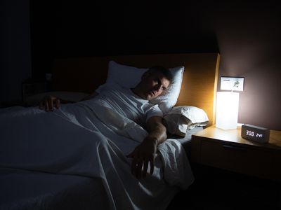 A man with insomnia looks at the clock at dawn from the bed with concern